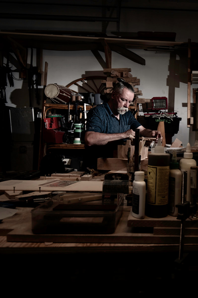 A woodworker looks closely at an instrument he is making.