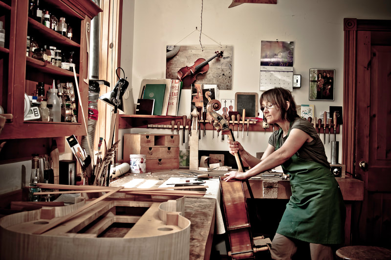 A young woman examines her repair to a century old cello.